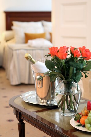 A bed with white bedding and a wooden headboard, a vase with orange roses, a champagne bottle, and a plate of fruit on a wooden table. - Hestia Hotel Radi un Draugi (Riga)