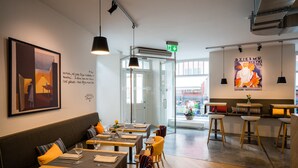 Un interior de restaurante con mesas de madera, bancos acolchados y lámparas colgantes.