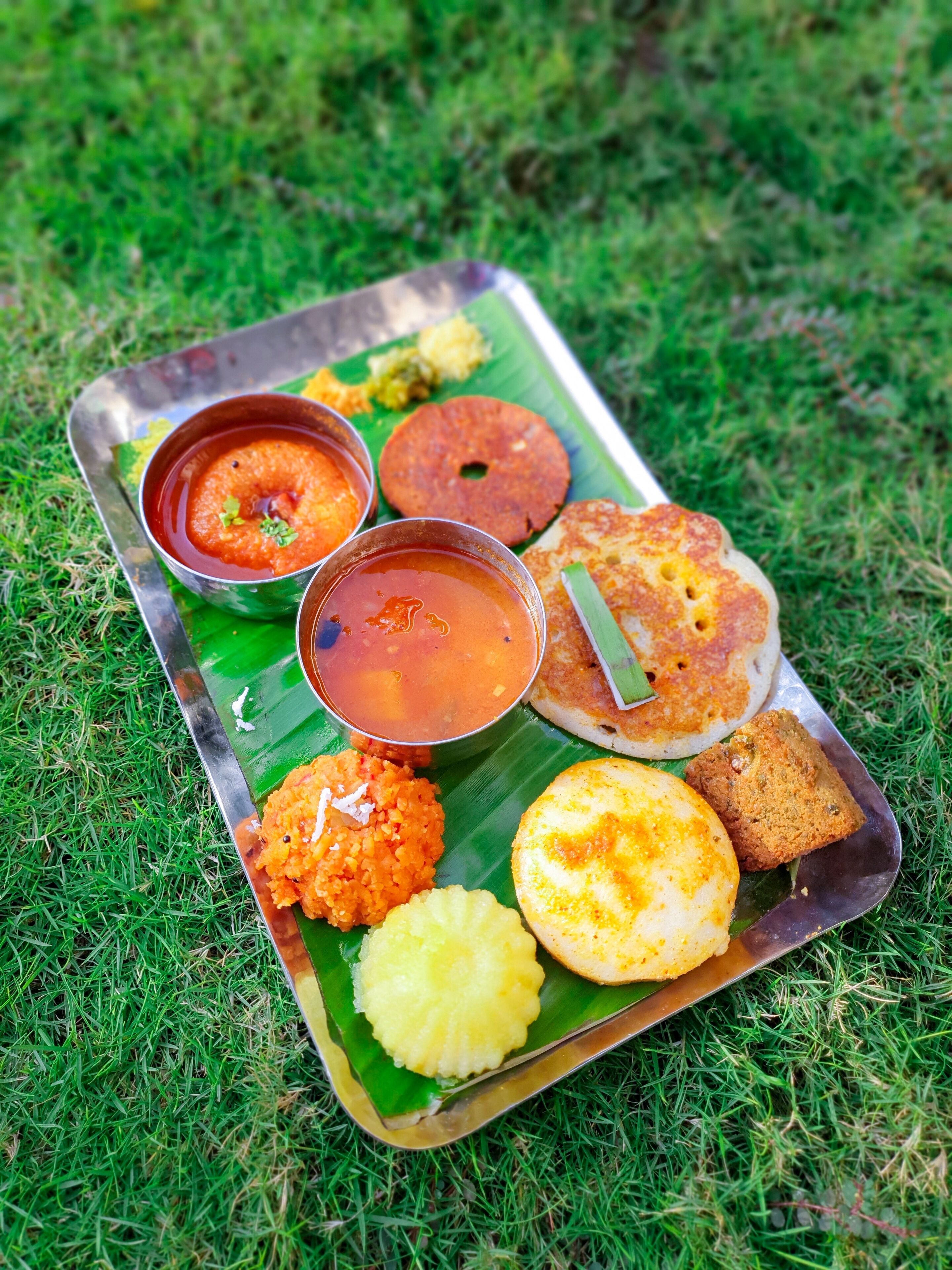 Una bandeja con varios platos de la cocina india, incluyendo una dosa, un tazón de sopa y otros acompañamientos sobre una hoja verde.