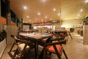 Un restaurante espacioso con mesas y sillas de madera, un techo alto con luces en forma de estrella y una pared de ladrillo al fondo.