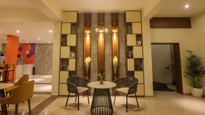 Un vestíbulo con mostrador de recepción, dos mesas redondas con sillas, una pared decorativa con estantes y una araña.