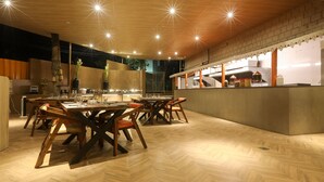Un restaurante moderno con suelo de madera, un área de comedor central con mesas y sillas, y una cocina visible al fondo.