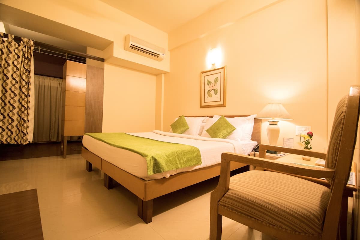 A hotel room with a bed, a chair, a lamp, and a wall-mounted air conditioner.