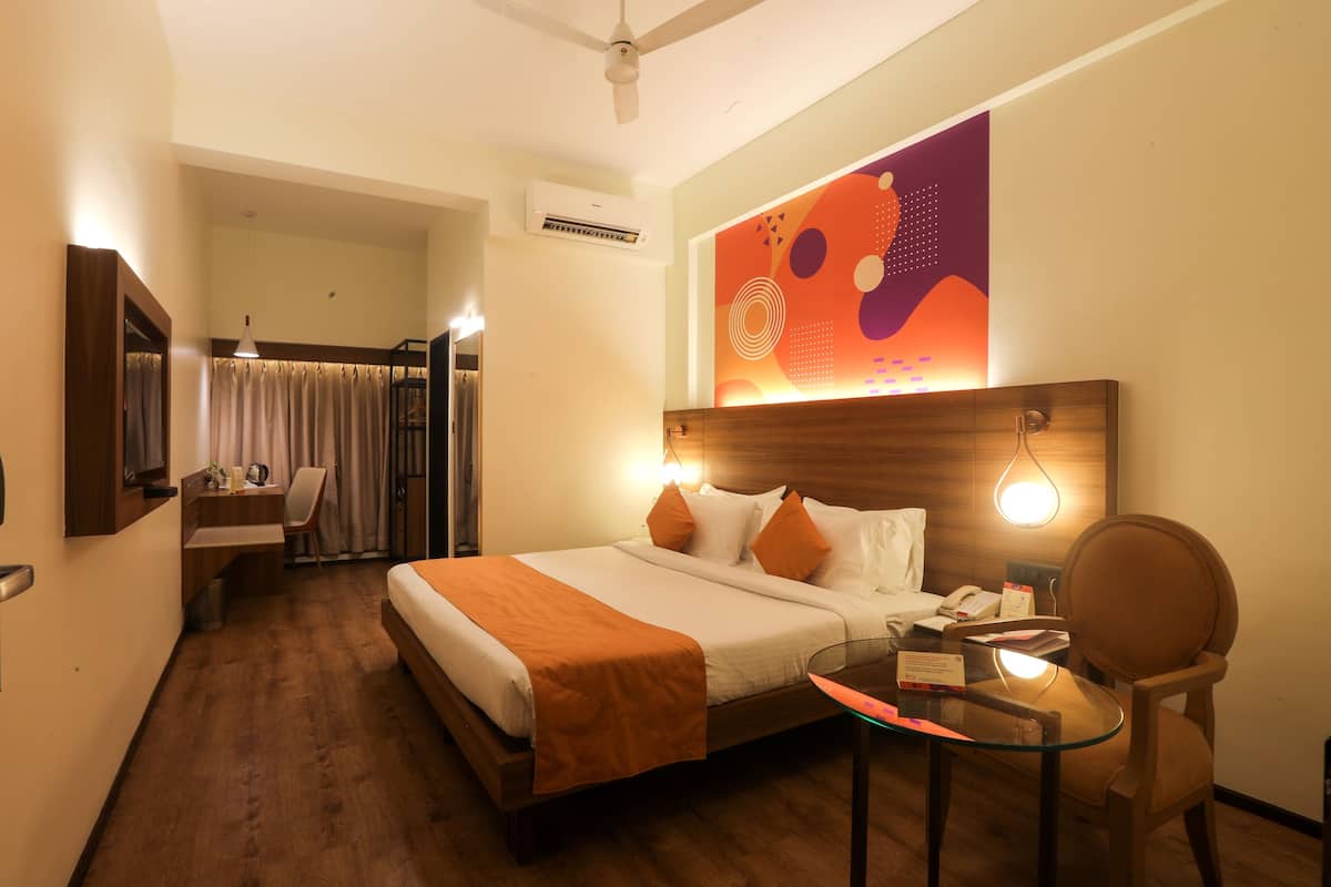 A hotel room with a bed, a desk, a chair, a table, a ceiling fan, and a wall-mounted air conditioner.