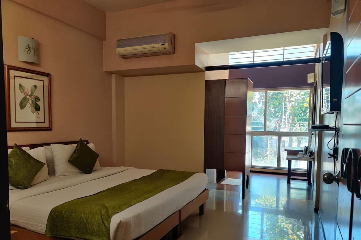 A bedroom with a bed, a window, an air conditioning unit, and a wall-mounted TV.