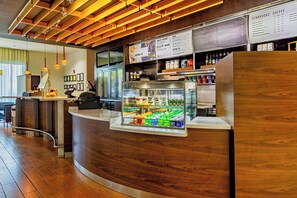A modern coffee shop interior with a wooden counter, a refrigerated display case, and a menu board. - Courtyard by Marriott Biloxi North/D'Iberville (D'Iberville)