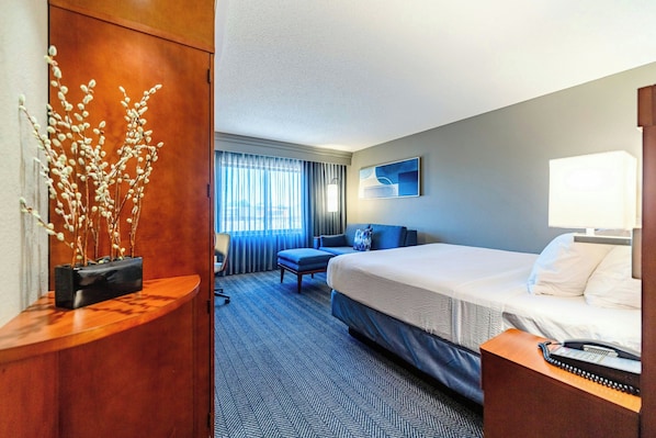 A hotel room with a bed, a desk, a chair, a sofa, a lamp, and a window with curtains.
