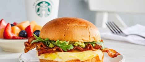 A breakfast sandwich on a plate with a cup of coffee in the background.