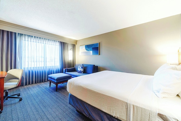 Une chambre d’hôtel avec un grand lit, un bureau, une chaise et une fenêtre avec des rideaux.