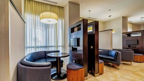 A modern hotel lobby with a curved seating area, a round table, and a television mounted on a wooden panel. - Courtyard by Marriott Biloxi North/D'Iberville (D'Iberville)