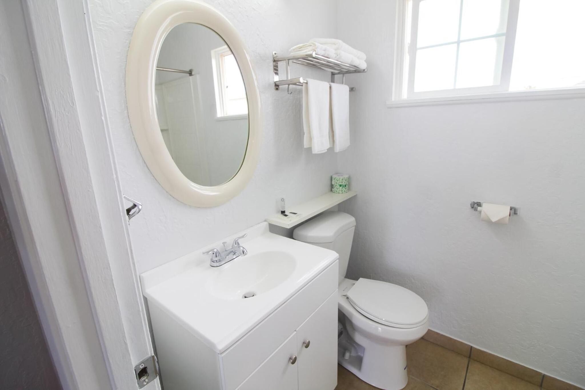 A white bathroom with a sink, mirror, toilet, and towel rack.