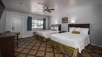 A hotel room with two beds, a desk, a ceiling fan, a window with curtains, and a patterned carpet.
