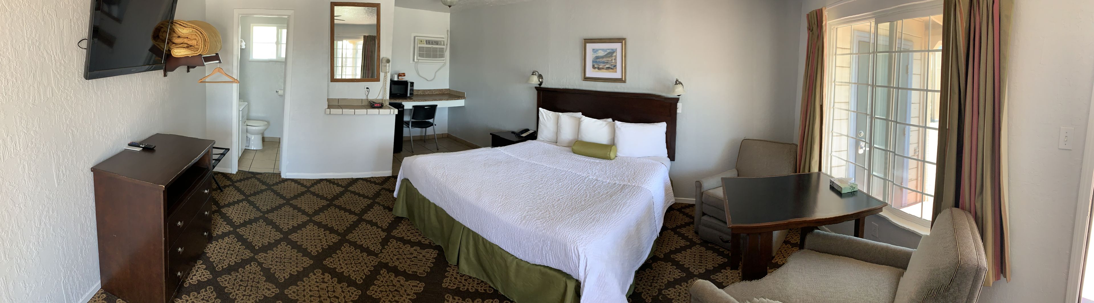 A hotel room with a bed, a desk, a chair, a TV, a mirror, and a window.