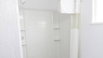Un espacio de ducha pequeño y blanco, cerrado con cortina, con un perchero y una ventana.