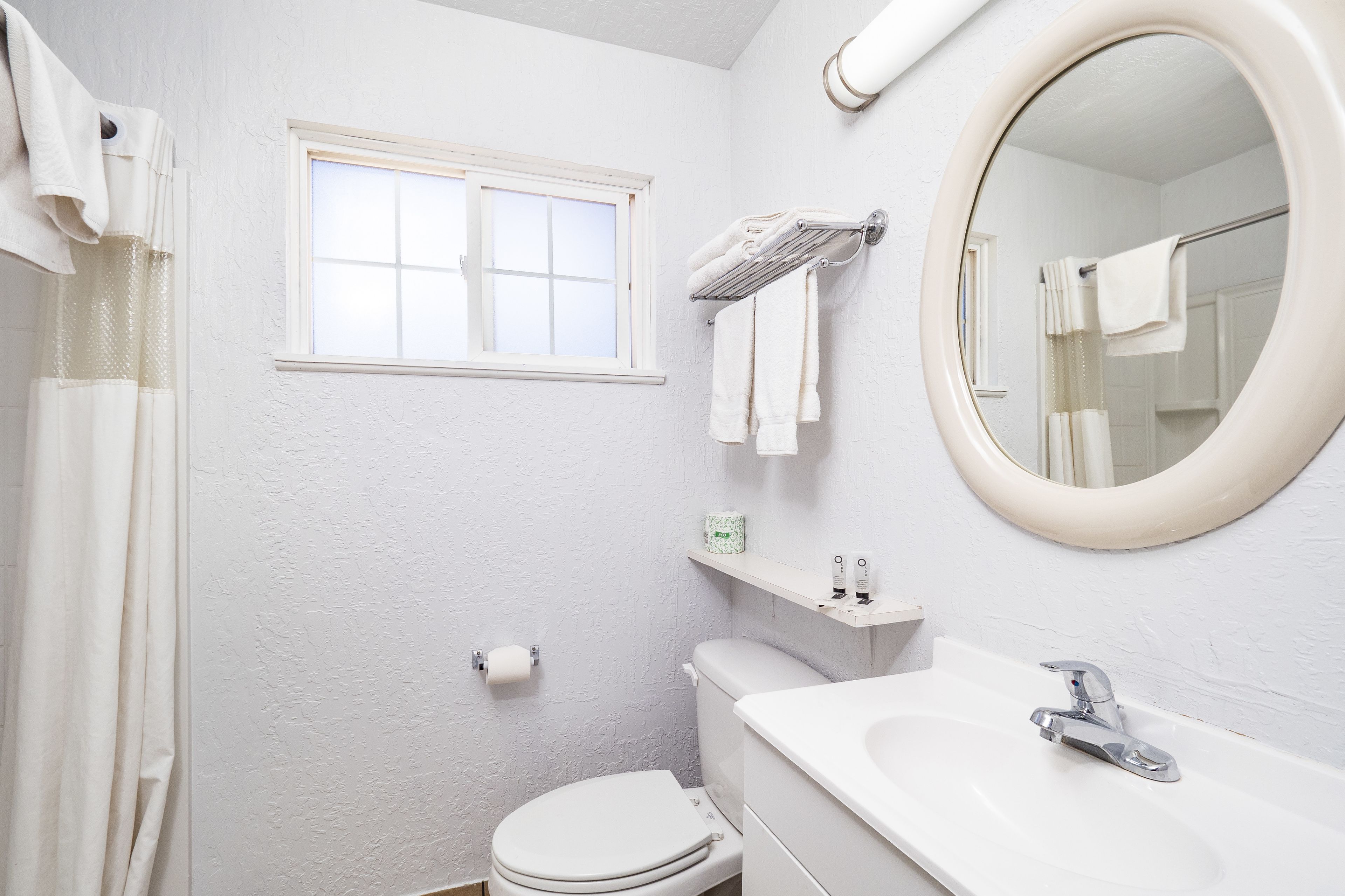 Un baño con inodoro, lavabo, espejo, toallero y ventana.