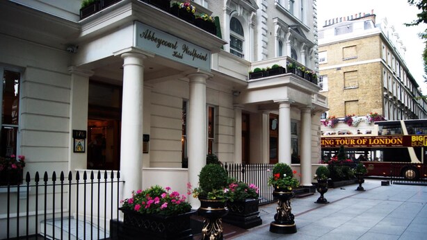 A historic building with columns, a sign reading "Abbey Court Westpoint," and a "Big Bus Tour of London" sign. - Aspen Apartments (London)