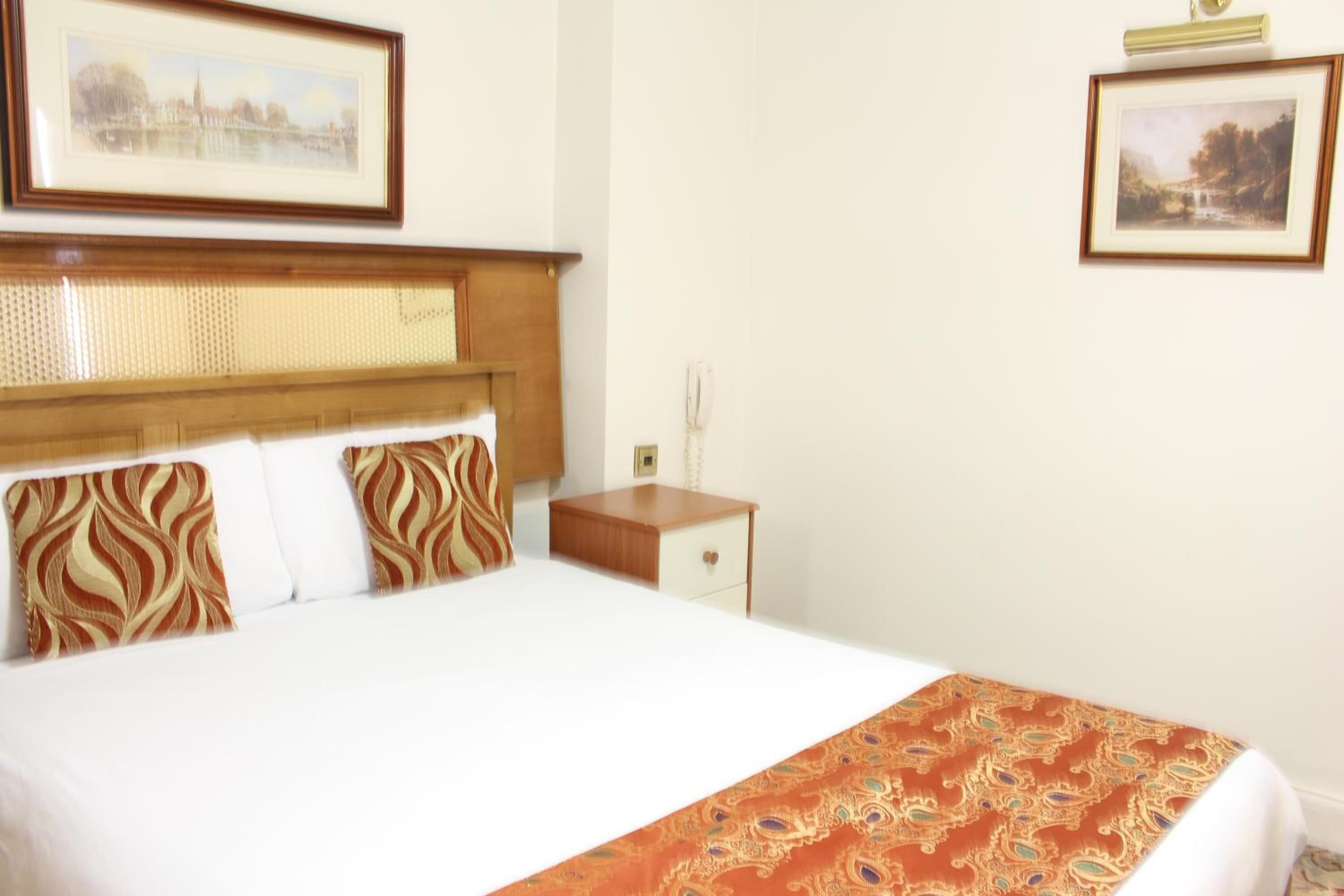 Uma cama bem arrumada com colcha estampada, cabeceira de madeira e dois quadros na parede.