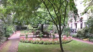 A garden with a paved path, a bench, and a flower bed. - Aspen Apartments (London)