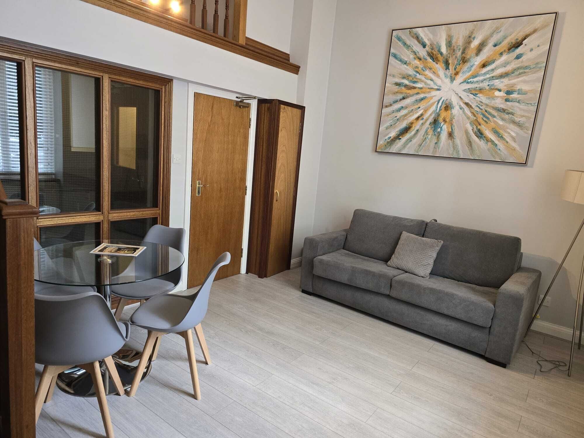 A modern living room with a grey sofa, two grey chairs, a glass table, and a wooden door.