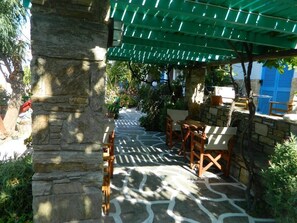 A covered outdoor seating area with stone pillars, a patterned stone floor, and wooden furniture. - Ioanna Apartments (Naxos)