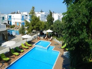 A swimming pool with lounge chairs and umbrellas, surrounded by greenery and white buildings. - Ioanna Apartments (Naxos)