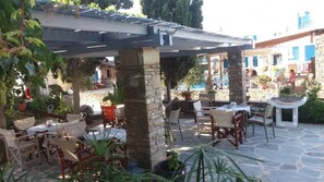 An outdoor patio with stone pillars, tables, and chairs. - Ioanna Apartments (Naxos)