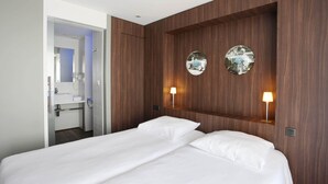 Hotelkamer met een wand van hout, twee bedlampen, een bed met witte lakens en een spiegel boven de wastafel.
