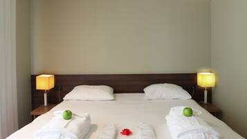 A neatly made bed with white linens, two bedside lamps, and two green apples on towels.