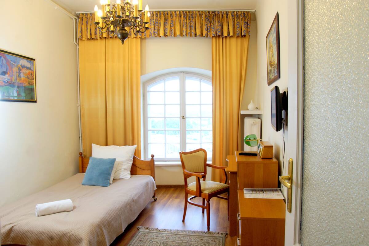 Een slaapkamer met een bed, een stoel, een bureau en een raam met gordijnen.