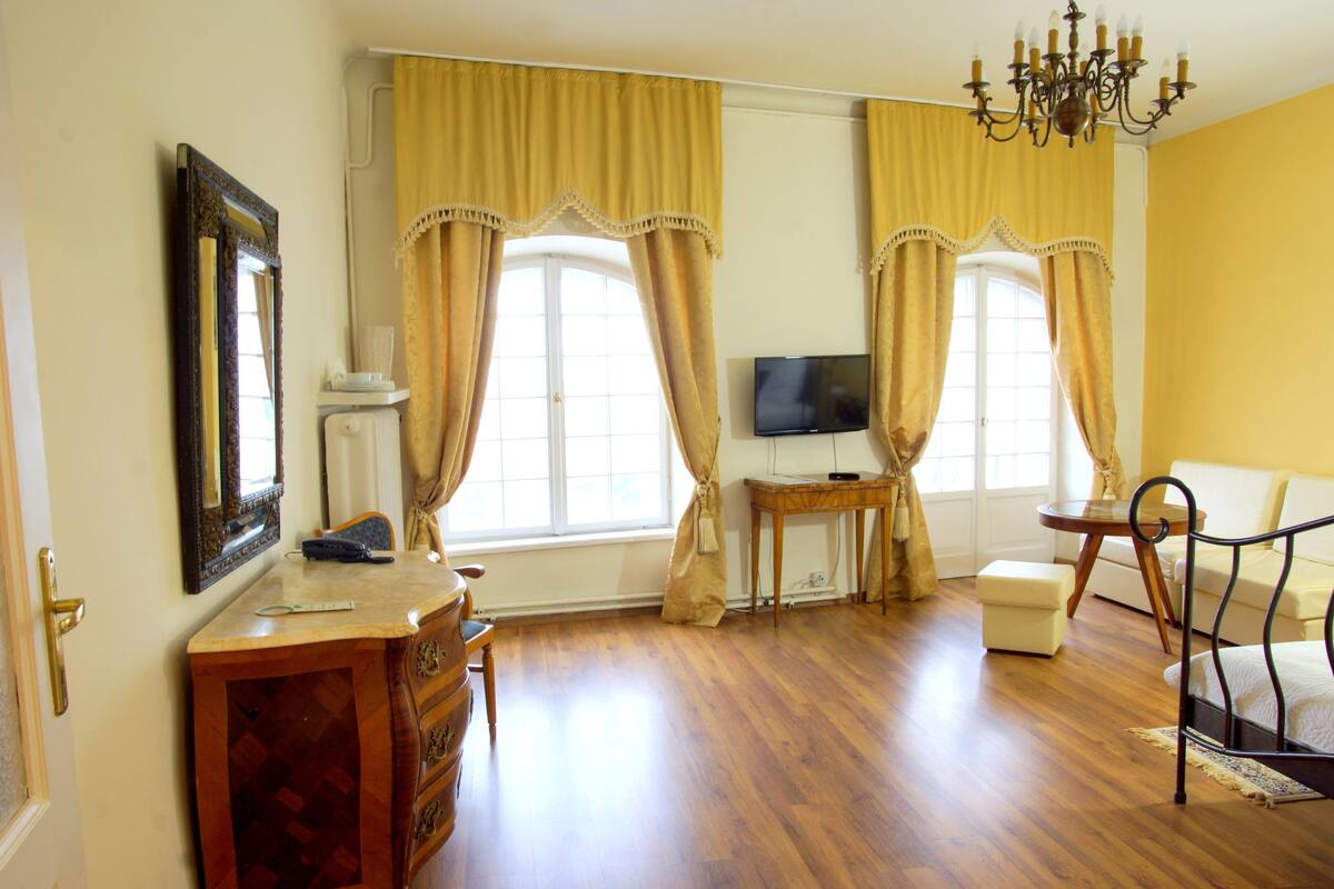 Een kamer met houten vloeren, een bureau met lades, een televisie op een standaard en een stoel.