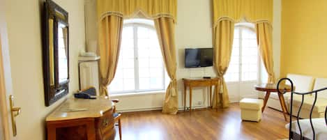 Une pièce avec un plancher en bois, un bureau avec des tiroirs, un téléviseur posé sur un meuble et une chaise.