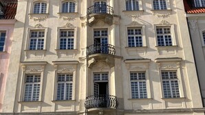 A historic building with ornate architectural details, including a central balcony with intricate ironwork, multiple windows, and a prominent entrance with a decorative door.