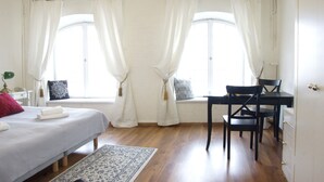 A bedroom with a bed, a desk, and two windows with curtains.