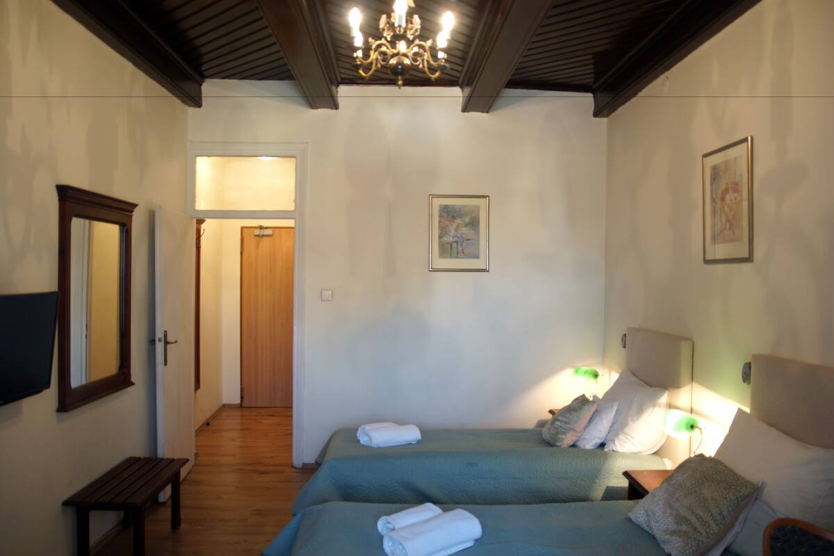 Een slaapkamer met twee bedden, een bankje, een kroonluchter en kunstwerken aan de wanden.