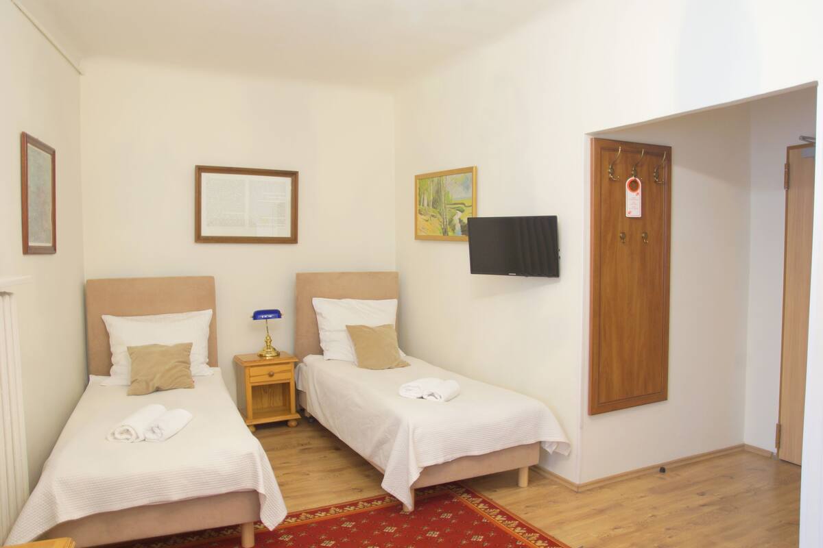 Een hotelkamer met twee enkele bedden, een houten garderobe, een flatscreen televisie en een klein nachtkastje met lamp.