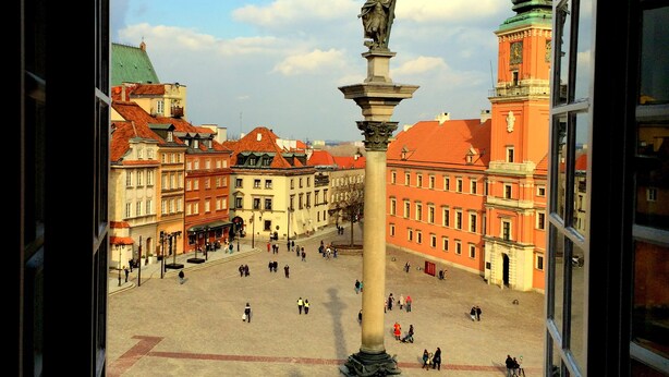 A view of a public square with a central monument, surrounding buildings, and a clear sky.