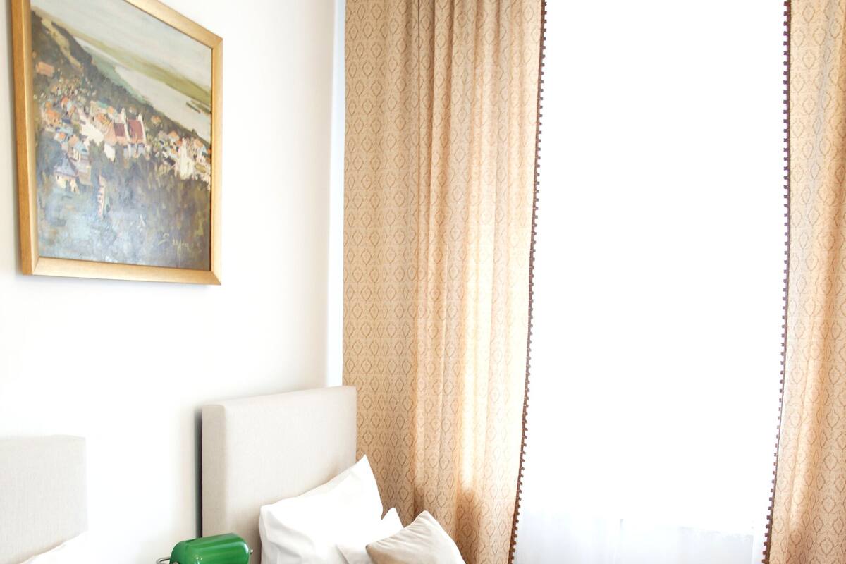 Een hotelkamer met twee bedden, een schilderij aan de muur en een raam met gordijnen.