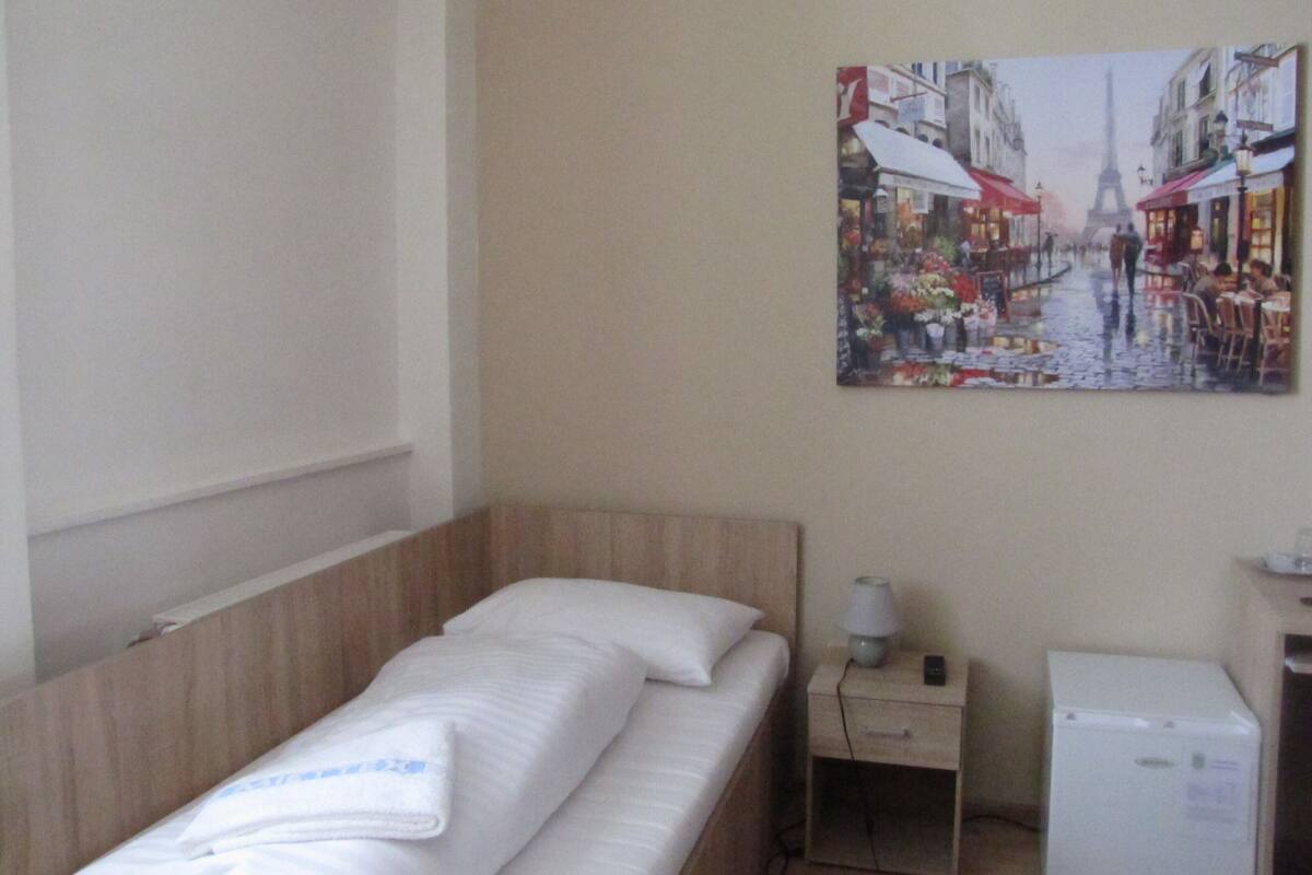 A hotel room with a bed, a nightstand, a lamp, and a small refrigerator.
