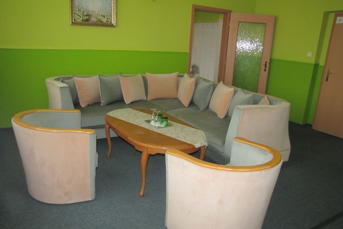 A room with a green wall, a grey sofa with cushions, a wooden coffee table, and two armchairs.