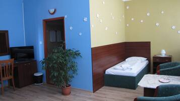 Una habitación con cama, escritorio, televisor, planta en maceta y una pequeña mesa con lámpara.