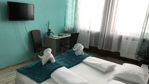 Una habitación de hotel con cama, escritorio, silla, televisión y ventana con cortinas.