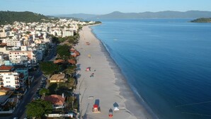 Vista aérea de un pueblo costero con una extensa playa arenosa, edificios a lo largo de la orilla y un mar azul cristalino.