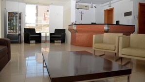 Un hall de hotel con mostrador de recepción, dos sillas negras, un sofá beige y una máquina expendedora.
