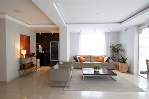 A modern living room with a sofa, armchairs, a coffee table, and a dining area with a table and chairs. - Luísa Studio Hotel (Florianópolis)