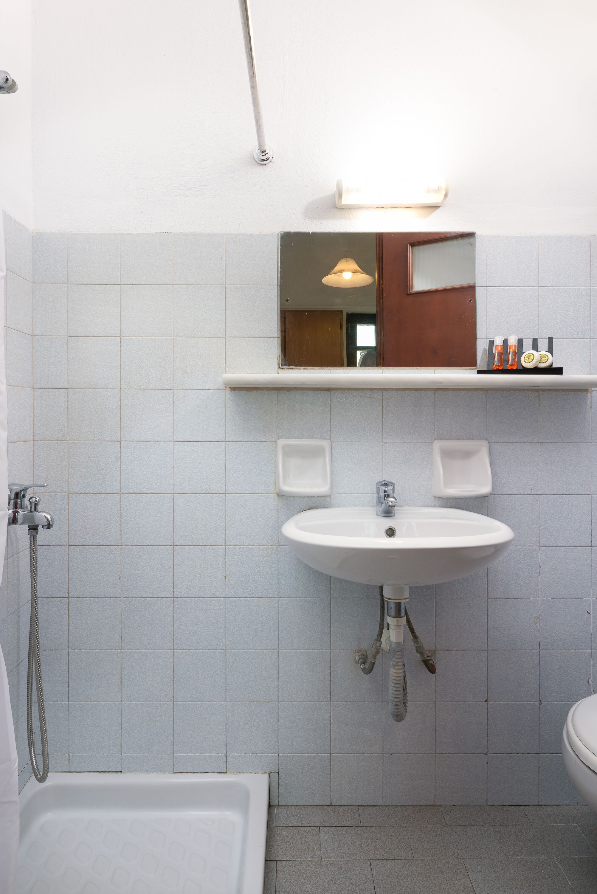 A bathroom with a white sink, mirror, and shower. There are soap dispensers on the wall and a towel rack.