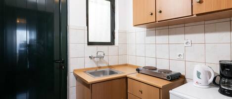 Cocina compacta con puerta negra, ventana, armarios de madera, un lavamanos, cafetera y refrigerador pequeño.