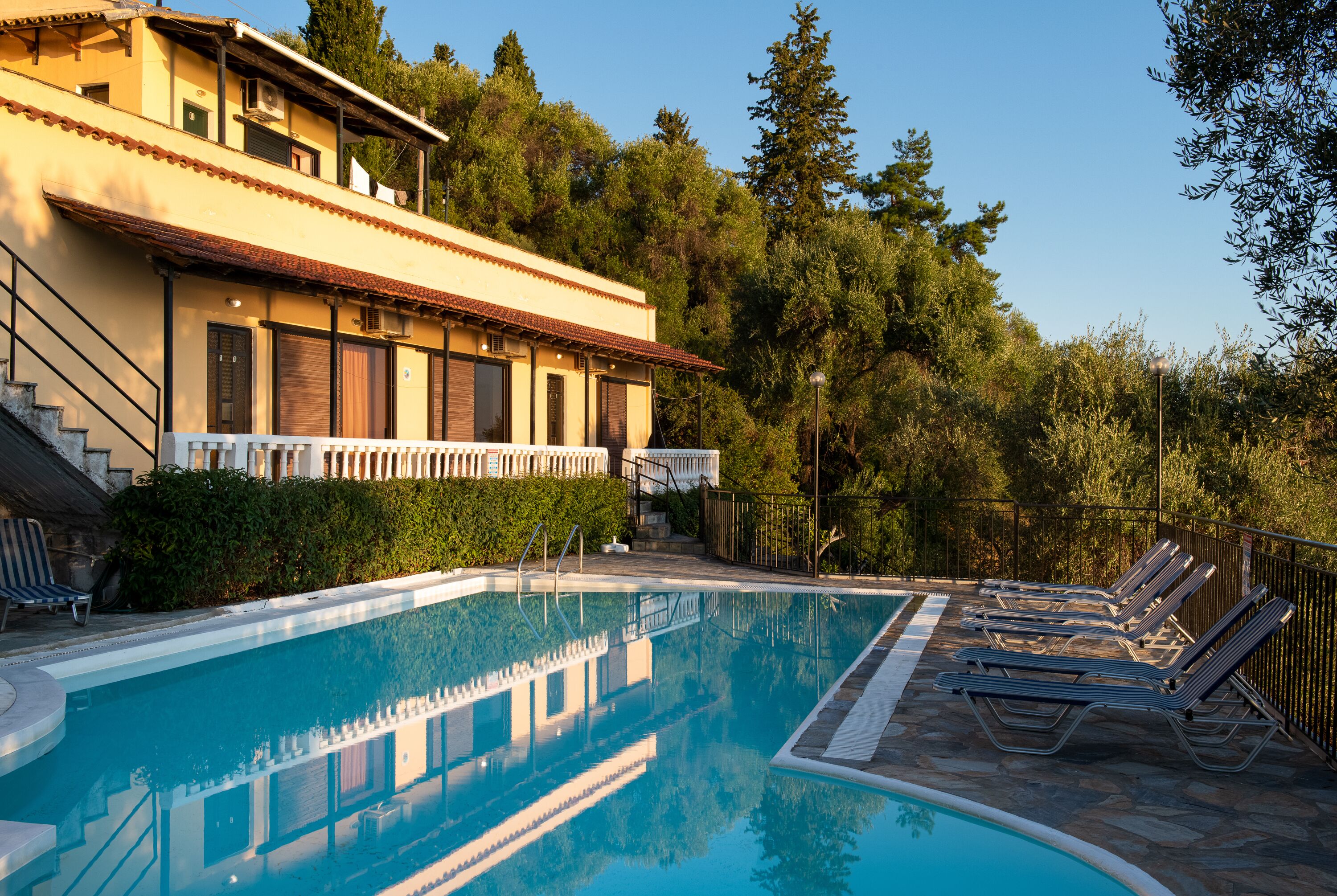 A pool area with lounge chairs, a staircase leading to a building, and a surrounding hedge.