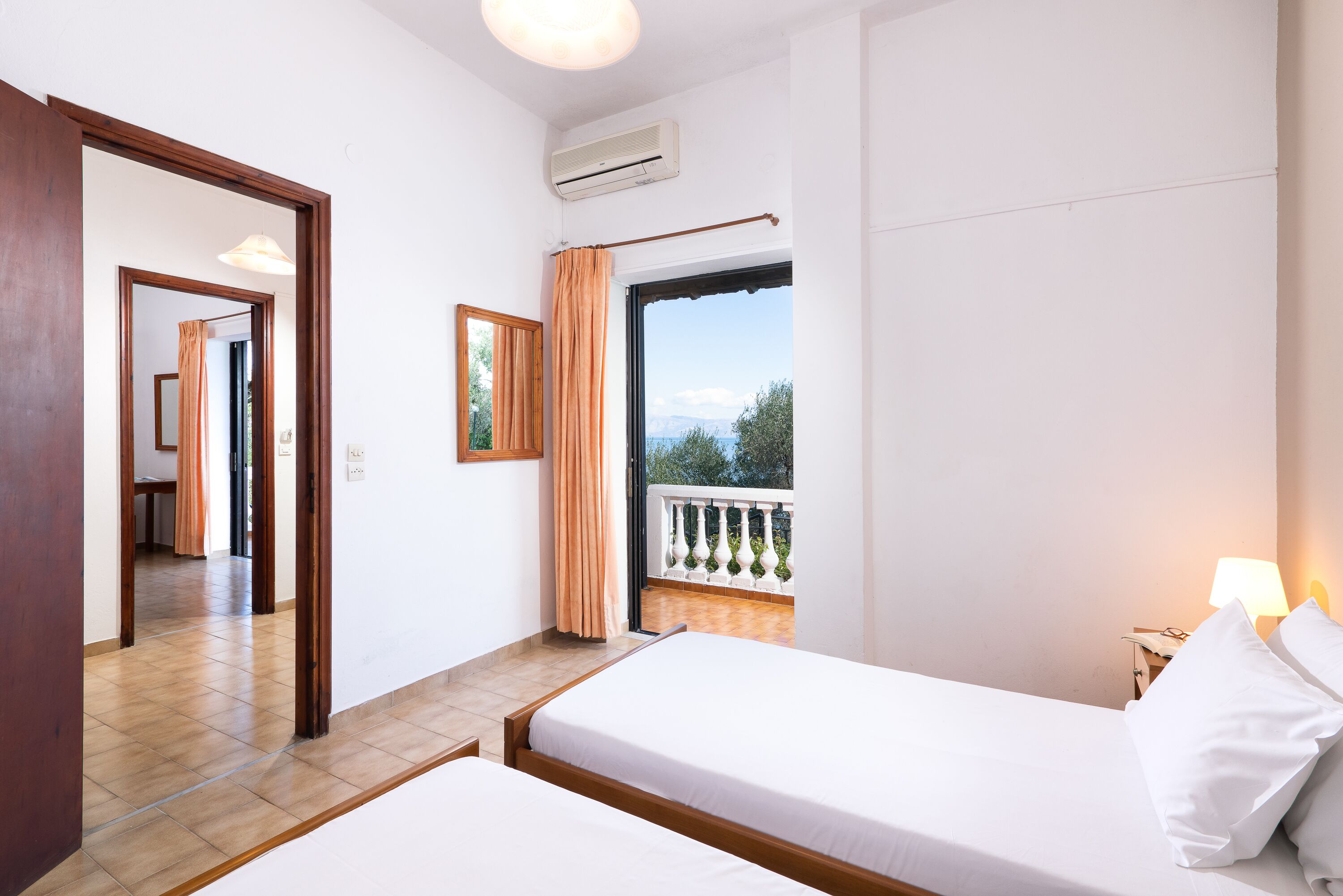 A hotel room with two beds, a balcony with a railing, and a view of the outdoors.