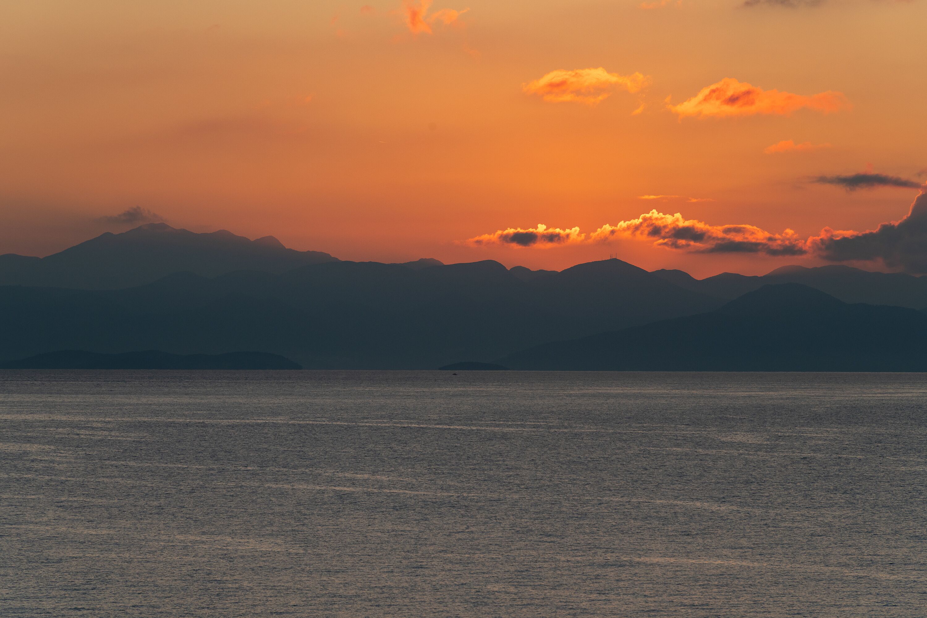 Een zonsondergang boven een kalme zee met verre bergen.