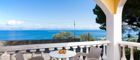Ein Balkon mit Tisch und Stühlen mit Blick auf eine Küstenlandschaft, Berge und das Meer.